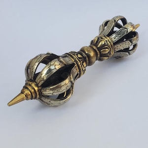 May include: A silver and gold metal vajra, a ritual object used in Buddhism and Hinduism. The vajra is a symbol of strength, power, and enlightenment. It is often used in ceremonies and rituals.
