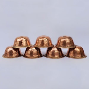 May include: A collection of eight copper-colored bowls with a hammered texture. The bowls are arranged in a pyramid shape, with a golden rim and a small hole at the top. The bowls are likely for serving or decorative purposes.