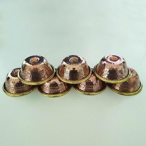 May include: Six small hammered copper bowls with brass rims. The bowls are stacked in a pyramid shape.