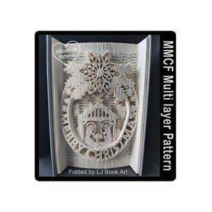 Puede incluir: Un libro blanco doblado en un diseño 3D de una escena navideña con una estrella, un pesebre y las palabras "Feliz Navidad". El libro se titula "MMCF Multi layer Pattern" y está doblado por LJ Book Art.