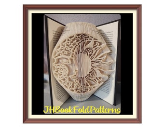 Può includere: Una scultura di arte di libro del sole e della luna, piegata dalle pagine di un libro. La scultura è esposta in una cornice marrone. Il testo "JHBookFoldPatterns" è visibile nella parte inferiore dell'immagine.