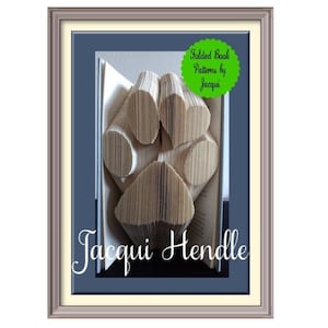 May include: A book with pages folded to create a paw print shape. The image includes a green circular badge with the text Folded Book Patterns by Jacqui and the name Jacqui Hendle written in white script at the bottom of the framed display.