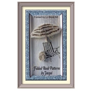 May include: A framed piece of book art featuring a beach chair and umbrella folded from the pages of a book. The art is titled "Folded Book Patterns by Jacqui" and "Folded by LJ Book Art".