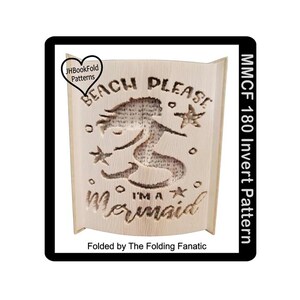 May include: A light-colored wooden book fold with a mermaid design. The text "BEACH PLEASE I'M A Mermaid" is cut out of the wood. The design includes starfish and the text "MMCF 180 Invert Pattern".