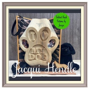 May include: A folded book art sculpture in the shape of a paw print with the words "I love my dog" carved into it. The sculpture is displayed on a table with a black and white patterned fabric and a small black dog toy.