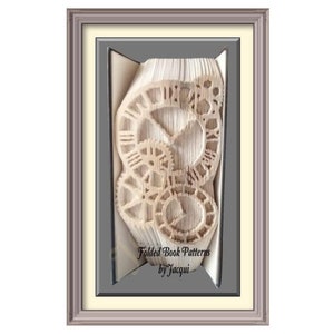 Op de afbeelding: Een ingelijst kunstwerk met een boek dat is gevouwen tot een driedimensionaal ontwerp van wijzerplaten en tandwielen. Het kunstwerk is getiteld "Folded Book Patterns by Jacqui".