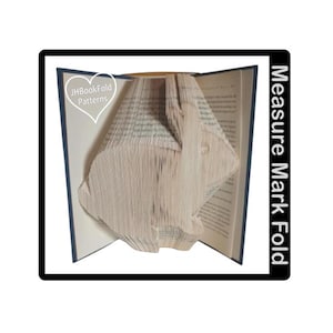 May include: A book with pages folded into a 3D design. The book is open and the folded pages are visible. The text "Measure Mark Fold" is printed on the right side of the book.