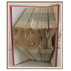 May include: A book with the word "JOY" folded into the pages. The letters are made of wood and have a rustic look. The book is open and the pages are folded in a way that creates the letters. The book is red and has a white spine.