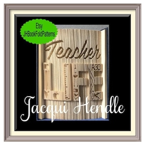 May include: A brown book with the words "Teacher Life" folded into the pages. The book is framed in a black frame with a white mount. The artist's name, "Jacqui Hendle", is written below the book.