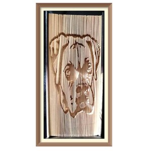 May include: A framed book art piece featuring a detailed, three-dimensional portrait of a boxer dog's face. The dog's fur is depicted in shades of brown, and its eyes are black. The artwork is created by folding the pages of a book.