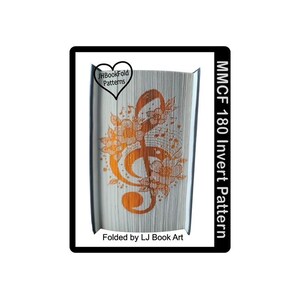 Peut inclure: Un livre plié en forme de clé de sol avec des accents floraux. Le livre est orange et blanc et le texte sur le côté indique "MMCF 180 Invert Pattern" et "Folded by LJ Book Art".