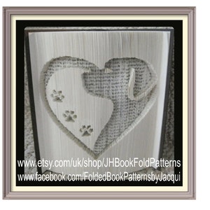 May include: A framed book art piece featuring a heart shape with a dog silhouette and paw prints cut into the pages. The artwork is in shades of white and gray, with visible text from the book pages. The frame is a light gray color.