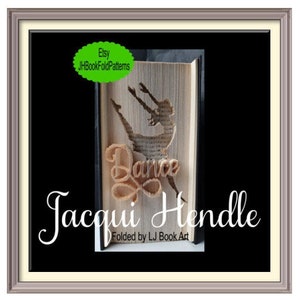 Könnte beinhalten: Eine Buchkunstskulptur einer Tänzerin mit dem Wort "Dance", das in das Buch gefaltet ist. Die Skulptur ist in einem silbernen Rahmen gerahmt und trägt den Namen der Künstlerin "Jacqui Hendle" sowie den Text "Folded by LJ Book Art" unterhalb der Skulptur.