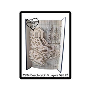 May include: A folded book art sculpture featuring a beach cabin, stairs, and two boats on the water, with pine trees in the background. A heart-shaped logo reads JHBookFold Patterns Folded by LJ Book Art. Text below reads 2934 Beach cabin 5 Layers 595 23.