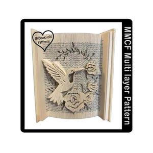 Könnte beinhalten: Ein Buchfaltkunstwerk mit einem Kolibri und Rosen. Das Design ist in die Seiten geschnitzt, mit dem Text "JHBookFold Patterns" in einem herzförmigen Logo. Der Text "MMCF Multi layer Pattern" befindet sich auf der rechten Seite.