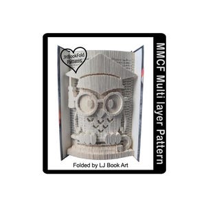 May include: A white paper owl wearing a graduation cap, folded into a 3D book art sculpture. The sculpture is titled "MMCF Multi layer Pattern" and is folded by LJ Book Art.