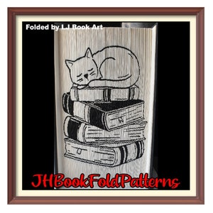 May include: A black and white illustration of a cat sleeping on top of a stack of books. The image is folded into a book shape and framed in a brown wood frame. The text "Folded by L.I Book Art" and "JHBookFoldPatterns" are visible in the image.