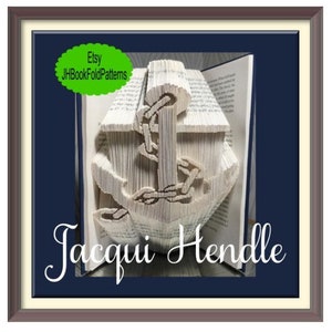 Op de afbeelding: Een wit boek gevouwen in de vorm van een anker met een ketting. Het boek is ingelijst in een bruin frame met een blauwe achtergrond. De tekst "Etsy JHBookFoldPatterns" en "Jacqui Hendle" zijn zichtbaar in de afbeelding.