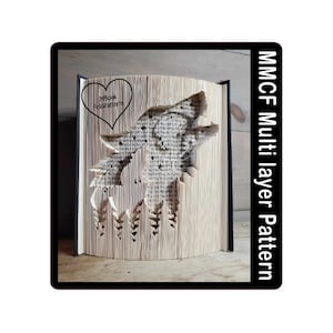 May include: A book with a wolf howling at the moon carved into the pages. The book is standing upright and has a black spine. The text "Book Folding" is written in a heart shape on the front cover. The text "MMCF Multi layer Pattern" is written vertically on the right side of the image.