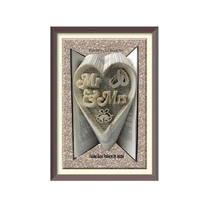 May include: A folded book art piece featuring a heart shape with the text Mr & Mrs, two rings, and two bells. The book is framed in a dark brown border with a glittery beige background. The text Folded by Lil Book Art and Folded Book Pattern by Jacqui is visible.