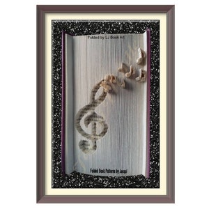 May include: A framed book art piece with a treble clef and musical notes folded from the pages of a book. The text on the book reads "Folded Book Patterns by Jacqui" and "Folded by LJ Book Art".