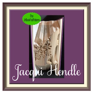 May include: A book sculpture with a silhouette of a woman and floral design carved into the pages. The book is displayed in a purple frame with the name "Jacqui Hendle" and an Etsy shop logo.