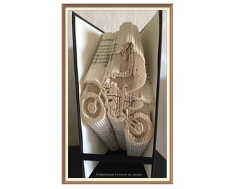 May include: A book folded into the shape of a person riding a dirt bike. The book is open and the pages are folded to create the shape of the bike and rider. The book is in a black frame.