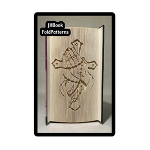 May include: A book with a folded paper design of praying hands with a rosary and a cross. The book is titled "JHBook FoldPatterns".
