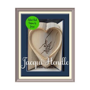 Puede incluir: Una escultura de arte de libro en forma de corazón con dos manos que se sostienen. La escultura está enmarcada en un marco plateado con un passe-partout azul. El texto "Folded Book Patterns by Jacqui" está en un círculo verde en la parte superior de la imagen. El texto "Jacqui Hendle" está en una fuente grande en la parte inferior de la imagen. El texto "Folded by LJ Book Art" está en una fuente más pequeña debajo del nombre.