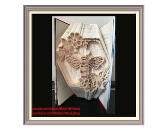 May include: A handcrafted book sculpture featuring a bee and honeycomb design. The artwork is created by folding the pages of a book, showcasing a detailed bee, flowers, and a honeycomb shape. The book is displayed in a frame.