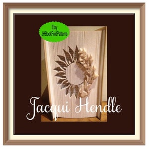 May include: A white book with a sunflower design folded into a 3D sculpture. The book is titled "Jacqui Hendle" and has a green label that says "Etsy JBookFoldPatterns".