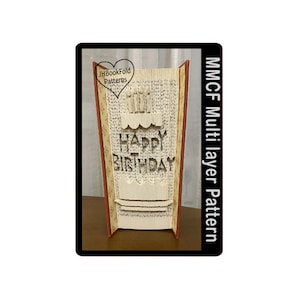 Puede incluir: Un libro con un diseño 3D pop-up de un pastel de cumpleaños con velas y las palabras "Happy Birthday". El libro es marrón con una encuadernación roja y se titula "MMCF Multilayer Pattern".