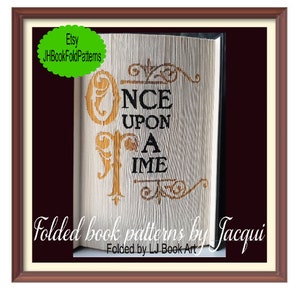 May include: A folded book art piece with the words "Once Upon A Time" in gold lettering on a white background. The book is folded into a 3D design and framed in a brown wood frame.