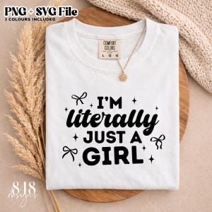 Op de afbeelding: Wit T-shirt met de tekst "I'M literally JUST A GIRL" in het zwart. Het shirt heeft een ronde hals en korte mouwen. Een gouden ketting met een zonvormige hanger ligt op het shirt. Het shirt ligt op een houten oppervlak.