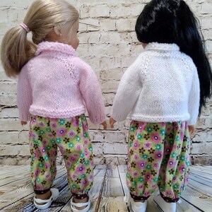 Puede incluir: Dos mu&ntilde;ecas con pantalones a juego de estampado floral y jers&eacute;is de punto. Una mu&ntilde;eca tiene el pelo rubio y lleva un jersey rosa. La otra mu&ntilde;eca tiene el pelo negro y lleva un jersey blanco.