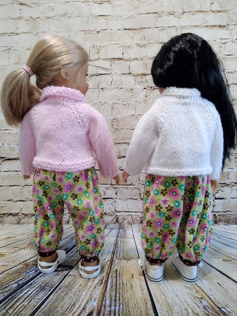 Puede incluir: Dos mu&ntilde;ecas con pantalones a juego de estampado floral y jers&eacute;is de punto. Una mu&ntilde;eca tiene el pelo rubio y lleva un jersey rosa. La otra mu&ntilde;eca tiene el pelo negro y lleva un jersey blanco.