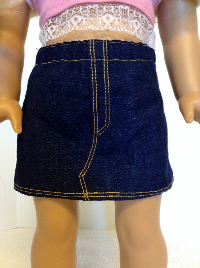 K&ouml;nnte beinhalten: Ein dunkelblauer Jeansrock mit gelben N&auml;hten. Der Rock hat ein klassisches Design mit Bund und einer Nahtdetail vorne. Der Rock ist f&uuml;r eine Puppe entworfen.