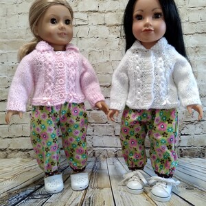 Puede incluir: Dos mu&ntilde;ecas con pantalones a juego de estampado floral y c&aacute;rdigans de punto. Una mu&ntilde;eca lleva un c&aacute;rdigan rosa y la otra un c&aacute;rdigan blanco.