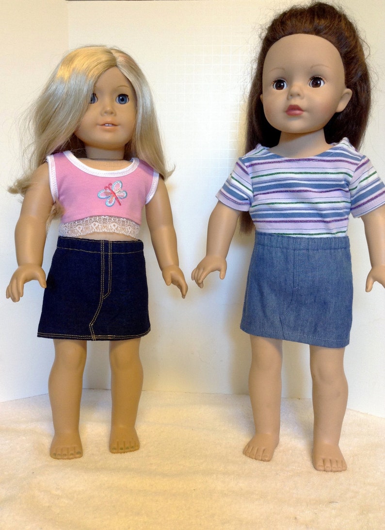 K&ouml;nnte beinhalten: Zwei Puppen in Jeansr&ouml;cken und Oberteilen. Eine Puppe hat blondes Haar und ein rosa Oberteil mit Schmetterlingsmuster und Spitzenbesatz. Die andere Puppe hat braunes Haar und ein gestreiftes Oberteil.