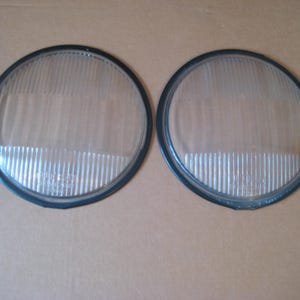 May include: Two round clear glass headlight lenses with black plastic trim.