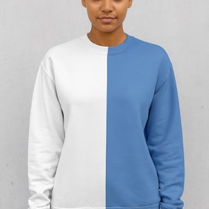 May include: A crew neck sweatshirt, split vertically into two colors. One side is white, and the other is a light blue. The sweatshirt is worn by a person with dark hair pulled back in a bun, against a light gray background.