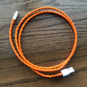 May include: An orange charging cable wrapped in a braided orange fabric. The cable has a white connector on each end.