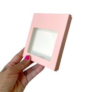 May include: A pink cardboard box with a clear window, perfect for packaging small items like jewelry or cosmetics.