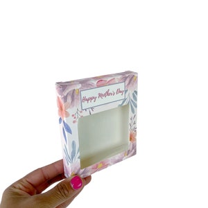 May include: A floral-patterned gift box with a rectangular window. The box features a watercolor design of pink, purple, and orange flowers with green leaves. The text "Happy Mother's Day" is displayed on a rectangular label.
