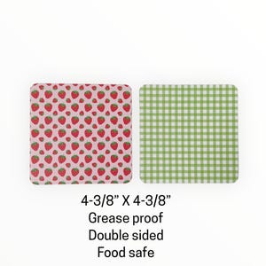 May include: Two square, double-sided food-safe coasters. One side features a pink background with a pattern of red strawberries. The other side has a green and white gingham pattern. Each coaster measures 4-3/8" x 4-3/8".
