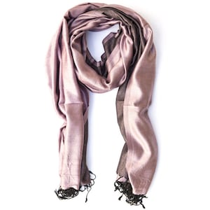 May include: A silky, mauve-colored scarf with a dark brown stripe and black fringe. The scarf is draped, showcasing its flowing fabric and texture. The scarf is a fashion accessory.
