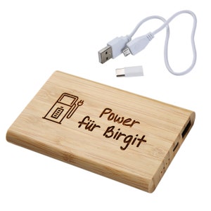 Könnte beinhalten: Eine Holz-Powerbank mit einem Benzinpumpen- und Stecker-Symbol und dem Text "Power für Birgit" auf der Vorderseite graviert. Die Powerbank wird mit einem weißen USB-Kabel und einem USB-C-Adapter geliefert.
