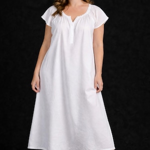 May include: A white nightgown with short sleeves and a V-neckline. The dress has a buttoned placket and a flowing skirt. The model is wearing the nightgown against a black background.