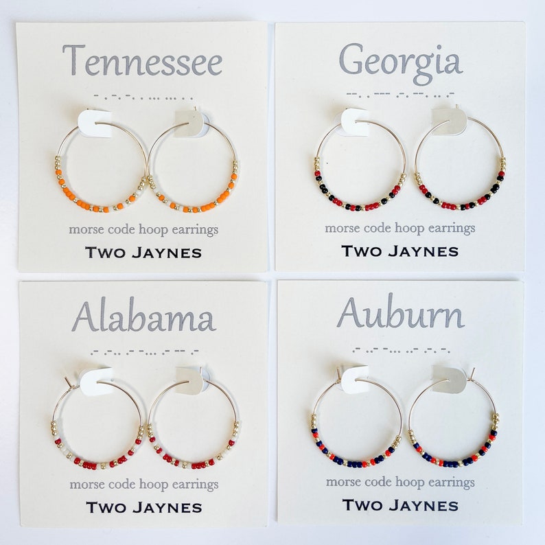 K&ouml;nnte beinhalten: Vier Karten mit verschiedenen College-Teamnamen und -farben. Jede Karte zeigt ein Paar silberne Creolen mit bunten Perlen. Die Karten lauten "Tennessee", "Georgia", "Alabama" und "Auburn". Jede Karte enth&auml;lt auch den Text "morse code hoop earrings" und "TWO JAYNES".