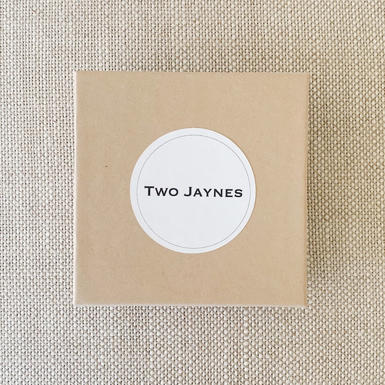 K&ouml;nnte beinhalten: Ein brauner Karton mit einem wei&szlig;en runden Aufkleber, auf dem in schwarzer Schrift "TWO JAYNES" steht.